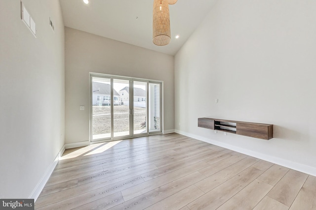 unfurnished living room with high vaulted ceiling, baseboards, visible vents, and wood finished floors