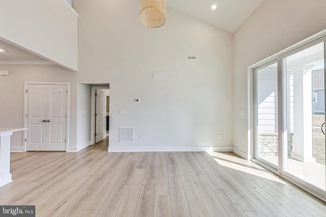 unfurnished room featuring light wood-style flooring, a high ceiling, and visible vents