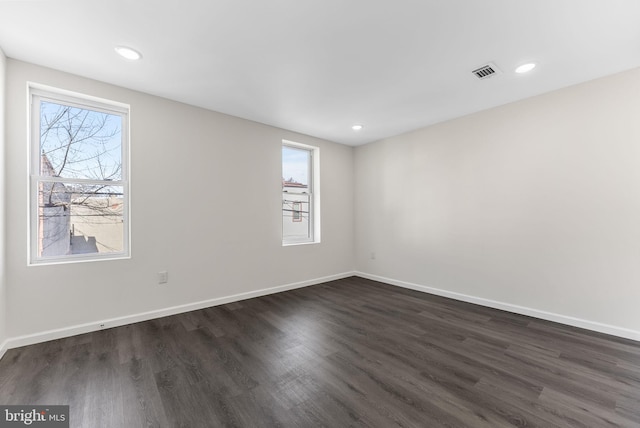 spare room featuring dark wood-style floors, plenty of natural light, visible vents, and baseboards