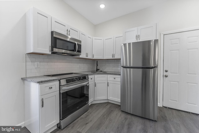 kitchen with dark wood-style floors, backsplash, appliances with stainless steel finishes, white cabinets, and a sink