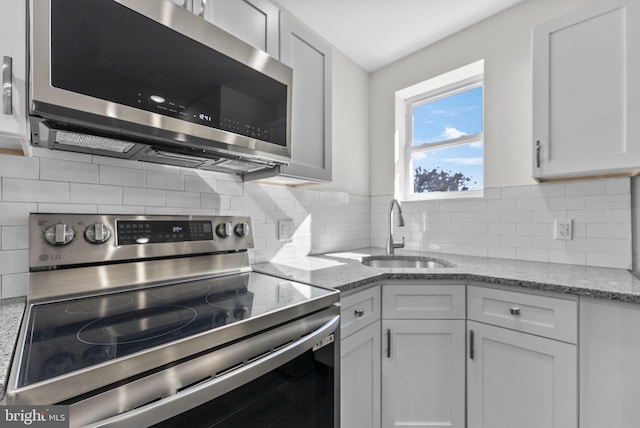 kitchen with light stone counters, appliances with stainless steel finishes, a sink, and white cabinetry