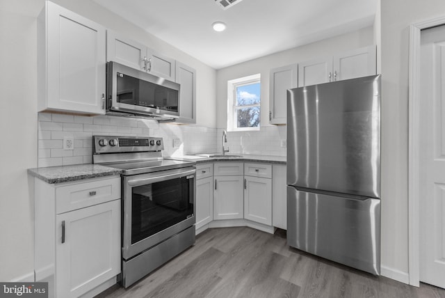 kitchen with stainless steel appliances, backsplash, a sink, and light wood-style flooring