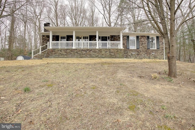 ranch-style home with brick siding, a porch, a chimney, an outbuilding, and a storage unit