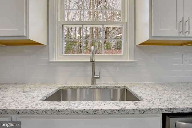 details featuring light stone counters, decorative backsplash, white cabinetry, and a sink