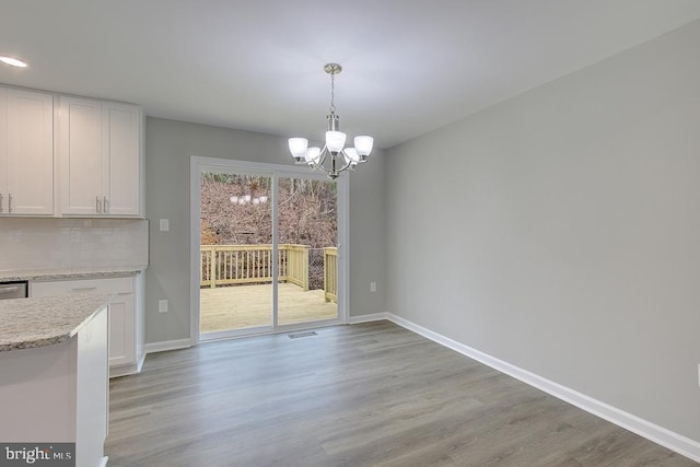 unfurnished dining area featuring baseboards, light wood-type flooring, and an inviting chandelier