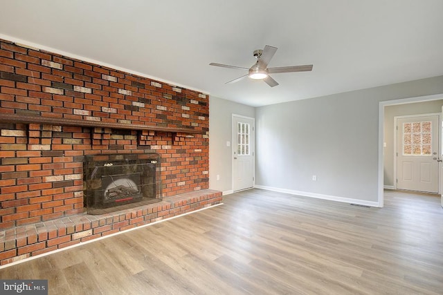 unfurnished living room featuring a wealth of natural light, light wood finished floors, baseboards, a brick fireplace, and ceiling fan