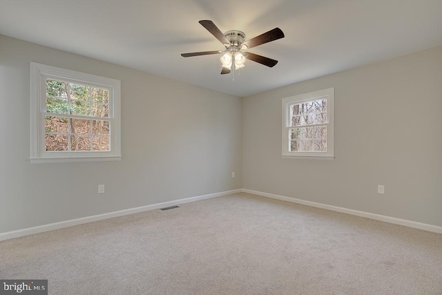 spare room with ceiling fan, light colored carpet, visible vents, and baseboards