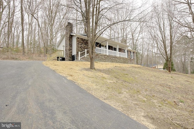 view of front of home featuring driveway, a porch, and a chimney