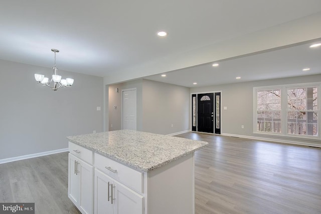 kitchen with baseboards, light wood finished floors, a kitchen island, white cabinets, and a chandelier