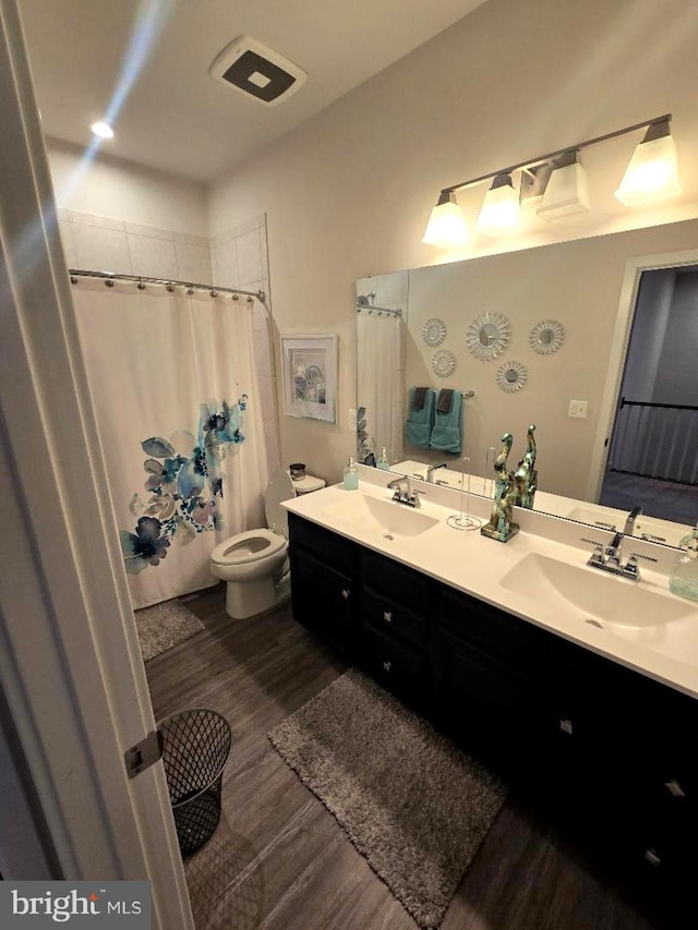 bathroom featuring double vanity, toilet, wood finished floors, and a sink