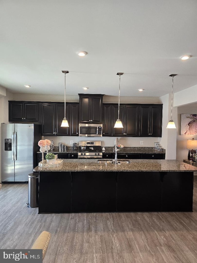 kitchen featuring dark cabinets, dark stone counters, light wood-type flooring, and stainless steel appliances