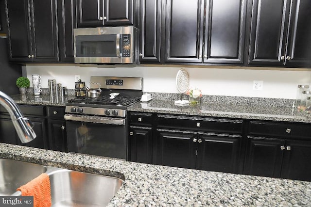 kitchen with light stone counters, stainless steel appliances, and dark cabinetry