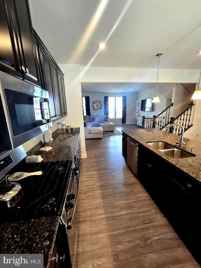 kitchen featuring dark stone countertops, a sink, stainless steel appliances, dark wood-type flooring, and dark cabinets