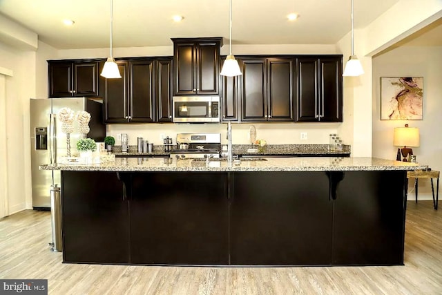 kitchen with an island with sink, light stone countertops, light wood-type flooring, and appliances with stainless steel finishes