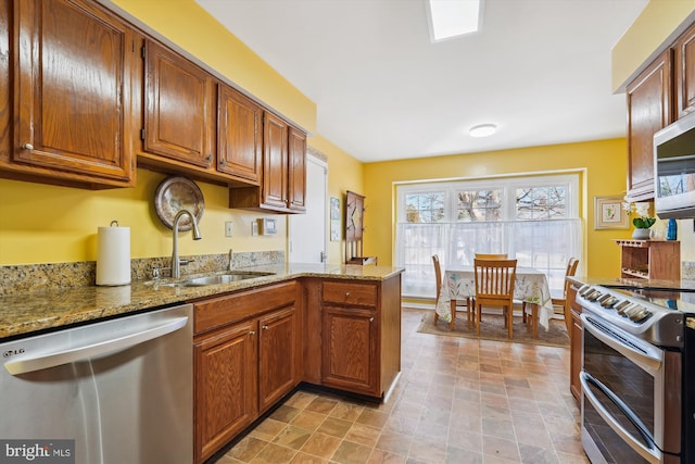 kitchen featuring light stone counters, brown cabinets, stainless steel appliances, and a sink