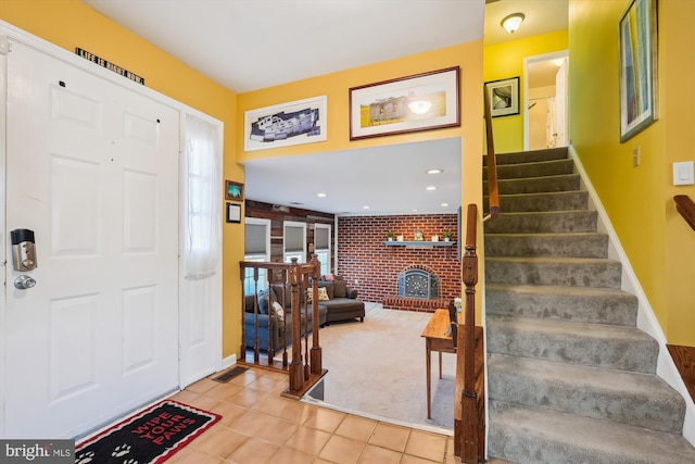 entryway with tile patterned floors, baseboards, a brick fireplace, and stairs