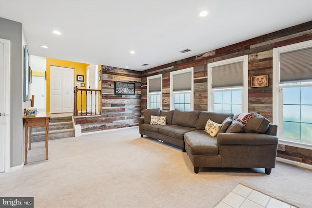 carpeted living room with stairs, recessed lighting, visible vents, and wood walls