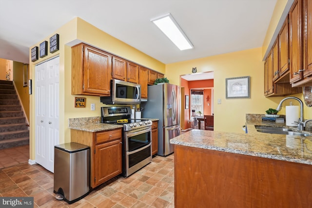 kitchen featuring light stone counters, brown cabinets, stainless steel appliances, and a sink