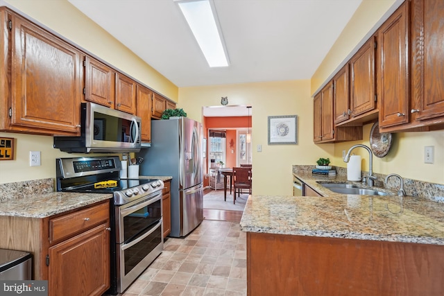 kitchen with a sink, light stone counters, appliances with stainless steel finishes, and brown cabinetry