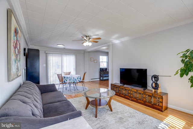 living area with a baseboard heating unit, crown molding, baseboards, and wood finished floors