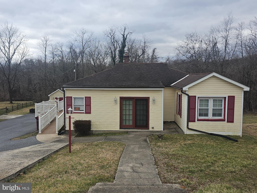 view of front facade with a chimney, roof with shingles, and a front yard