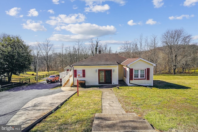 view of front of house featuring a front yard, fence, driveway, a shingled roof, and a chimney