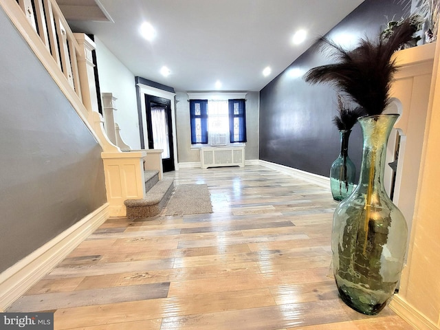 foyer featuring radiator, light wood-style flooring, baseboards, and stairs