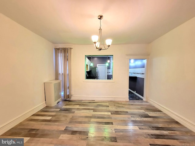 unfurnished dining area featuring a chandelier, baseboards, and wood finished floors