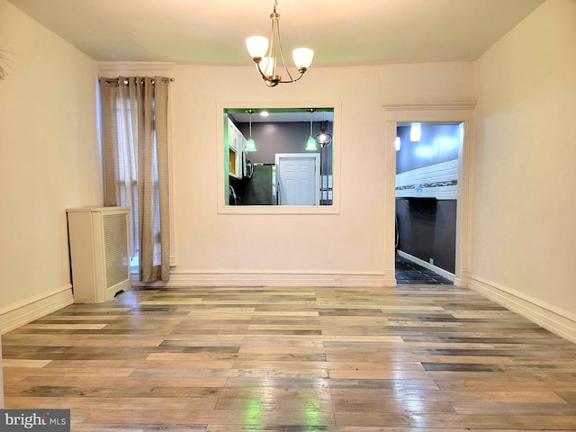 unfurnished dining area featuring a notable chandelier, baseboards, and hardwood / wood-style floors