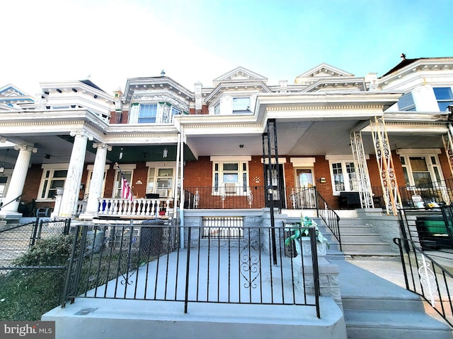 townhome / multi-family property featuring covered porch, brick siding, and a fenced front yard