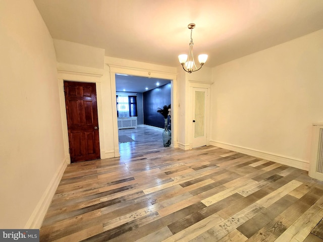 unfurnished dining area with a chandelier, hardwood / wood-style flooring, and baseboards