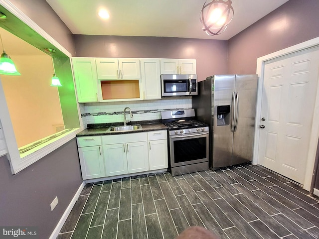 kitchen with a sink, appliances with stainless steel finishes, backsplash, wood tiled floor, and dark countertops