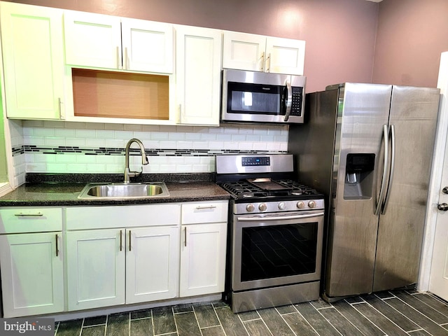 kitchen with wood finish floors, stainless steel appliances, tasteful backsplash, white cabinets, and a sink