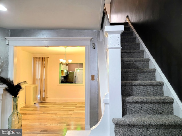 stairs with an inviting chandelier and wood finished floors