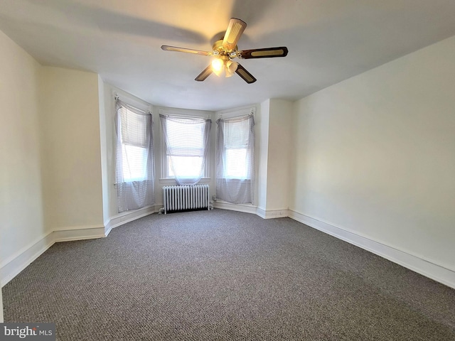 unfurnished room featuring ceiling fan, radiator heating unit, dark carpet, and baseboards