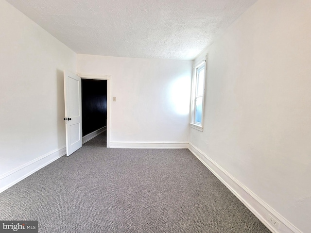 unfurnished room featuring a textured ceiling, dark carpet, and baseboards