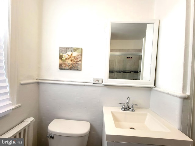 bathroom with tiled shower, toilet, vanity, and radiator heating unit