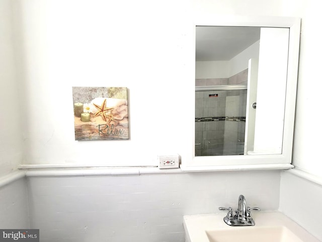 bathroom with a wainscoted wall, tiled shower, a sink, and tile walls