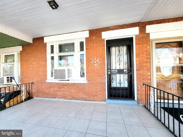 entrance to property with covered porch, cooling unit, and brick siding