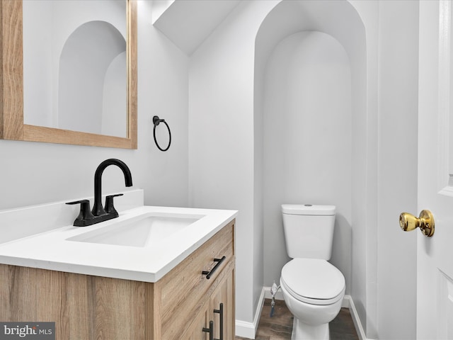 half bath featuring vanity, toilet, wood finished floors, and baseboards