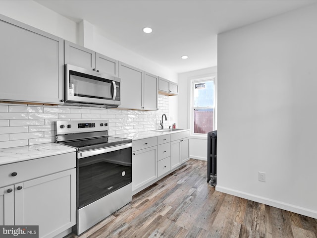 kitchen featuring backsplash, baseboards, light wood-type flooring, stainless steel appliances, and a sink