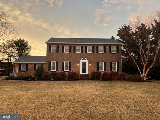 colonial inspired home featuring a yard, brick siding, and a chimney