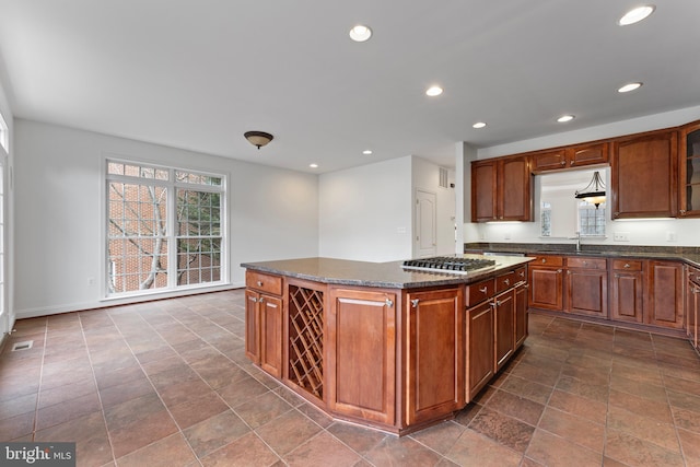 kitchen featuring glass insert cabinets, dark stone countertops, a center island, stainless steel gas stovetop, and recessed lighting