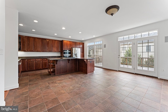 kitchen with stainless steel fridge with ice dispenser, dark countertops, a kitchen island, a kitchen breakfast bar, and recessed lighting