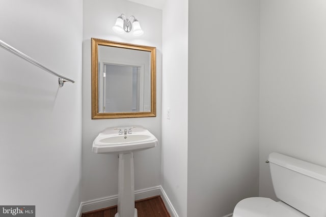 half bathroom with wood finished floors, a sink, toilet, and baseboards