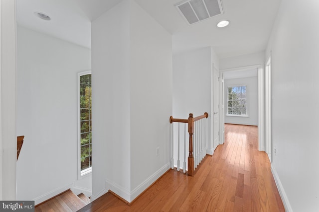 hall featuring light wood-style flooring, visible vents, baseboards, and an upstairs landing