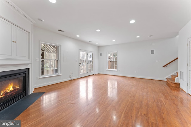 unfurnished living room with light wood-style flooring, recessed lighting, a fireplace with flush hearth, visible vents, and stairs