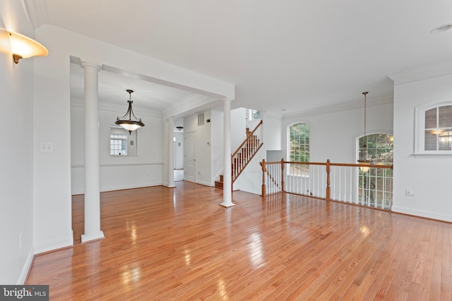 empty room featuring ornate columns, baseboards, light wood finished floors, and crown molding