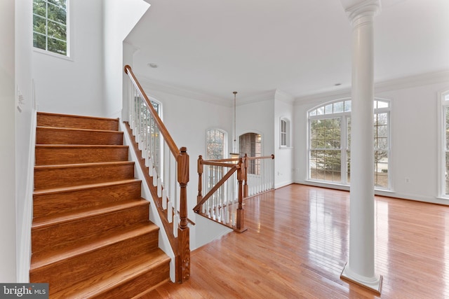 foyer entrance featuring ornamental molding, a healthy amount of sunlight, light wood-type flooring, and ornate columns