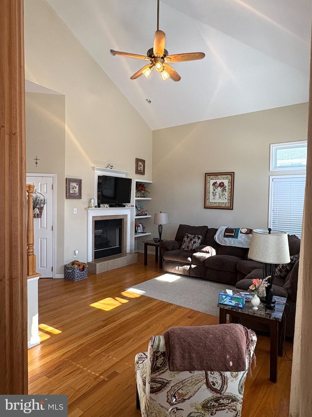 living area featuring high vaulted ceiling, a fireplace, wood finished floors, and a ceiling fan